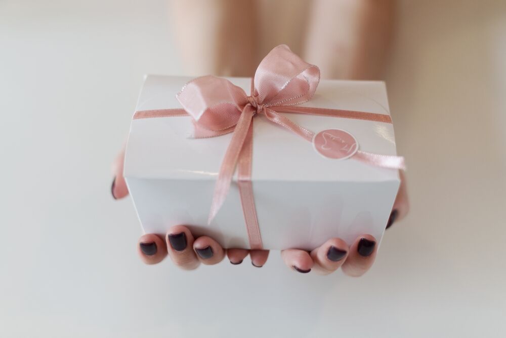 Hände halten ein verpacktes Geschenk mit rosé Schleife