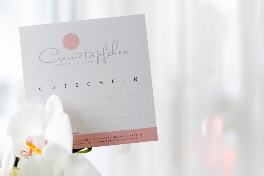 Gutschein des Cremetöpfchens vor einer weißen Orchidee